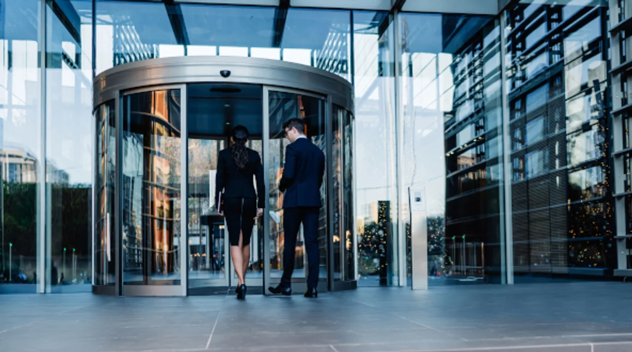 Two businesspeople entering a modern glass building through a revolving door