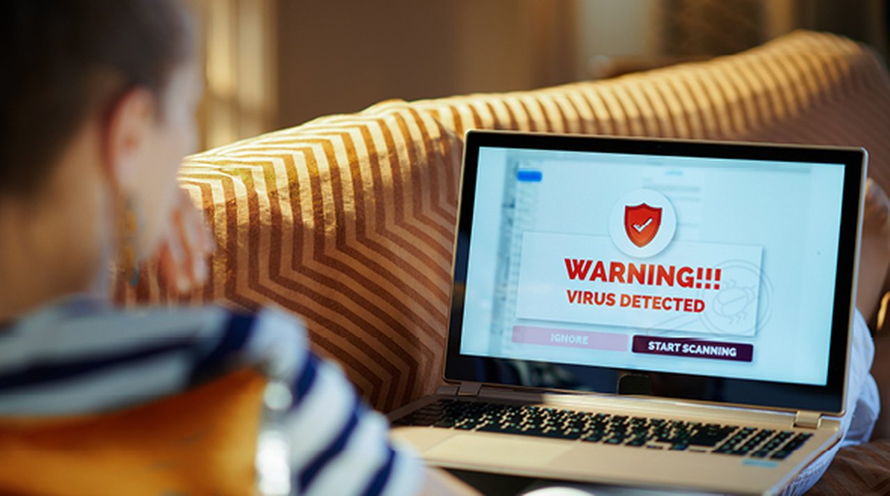 Laptop with a warning message on the screen, with a woman sitting in front of it on a sofa