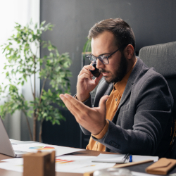 Businessman talking on the phone while checking his smartphone at an office desk