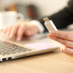Hand holding a USB flash drive near a laptop