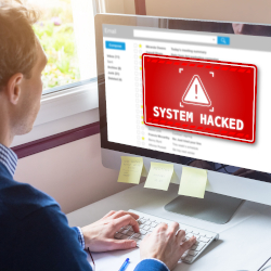 Person looking at a computer screen displaying a system hacked warning