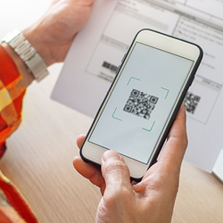 Eine Person scannt mit ihrem Smartphone einen QR-Code auf einem Papierdokument ein