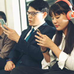 Two commuters using smartphones, with one wearing headphones