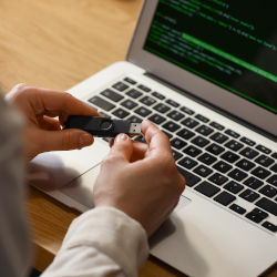 Person connecting a USB device to a laptop displaying source code
