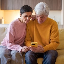 Two elderly people sitting on a sofa, leaning over a smartphone