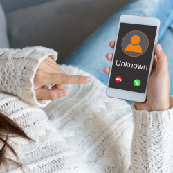 Eine Frau auf einem Sofa hält ein Smartphone in der Hand, auf dem ein Anruf einer unbekannten Nummer eingeht